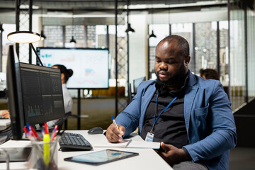 African american advisor takes notes to create a new growth strategy and fulfill project objectives at the office, writing data insights to forecast an international expansion. Productivity.