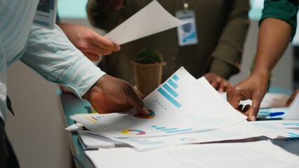 Multiethnic team reviewing analytics in a late night company briefing after hours, projections and data insights to align business goals with expectations in modern office space. Camera B.
