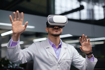 A man stands in a contemporary office wearing a virtual reality headset. He has his hands raised, interacting with virtual elements. The workplace features bright lighting and sleek design.