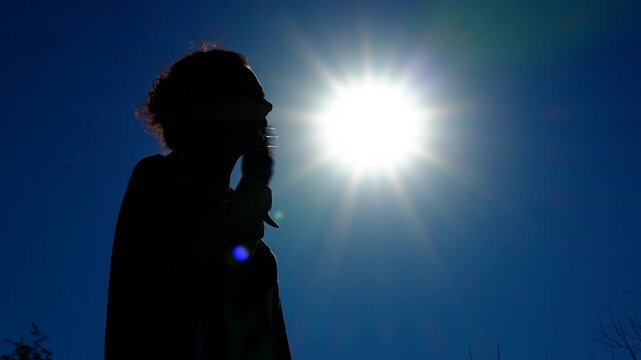 A woman suffers from the heat, waving her hand, making a breeze. Silhouette of a woman against the background of the summer sun