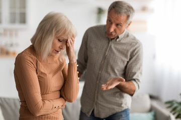 Man and woman are engaging in a serious discussion in a cozy living room. The woman shows signs of stress while the man gestures, trying to communicate his viewpoint.