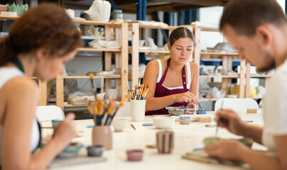 Pottery workers paint ceramic plates together at a table