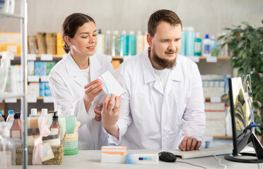 Man pharmacist at computer communicate with girl colleague. Employee discuss about treatment protocol, selects available drugs for treatment regimen
