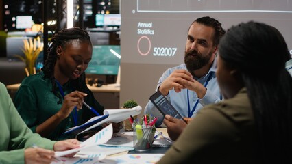 Business people prepare for a pitch by studying financial data on files reports inside the boardroom after hours. Exchanging insight and delivering forecasting updates for management. Camera B.