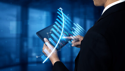 A business professional interacts with a tablet displaying digital financial graphs and analytics, showcasing modern technology use in a corporate environment. Scalp