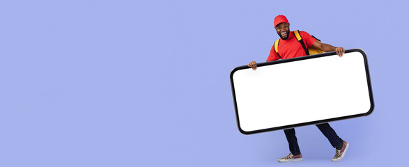 A cheerful young man stands holding a large blank sign, dressed casually in a red shirt and cap. He...