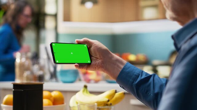Horizontal chroma key on phone with mature man enjoying retired life at home, relaxing at the kitchen table for breakfast. Space with homemade meal and coffee for good morning routine. Camera B.