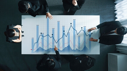 A diverse group of business professionals collaborates in a modern office setting, analyzing financial charts and data for strategic planning and decision-making. Scalp