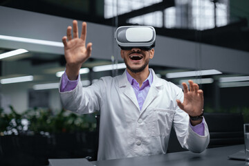 A man wears a virtual reality headset in an office environment. He raises his hands and smiles while interacting with the virtual world. The office is well-lit and modern.