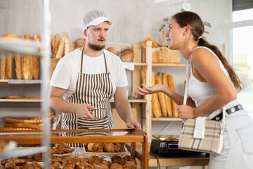 Concerned young man seller serves girl buying fresh croissants in bakery store
