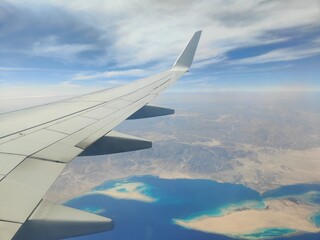 Aerial View of Airplane Wing Over Coastline and Sea, Red Sea, Egypt - A high-resolution aerial photograph taken from an airplane window, showing the aircraft wing above a deep blue sea with a desert c