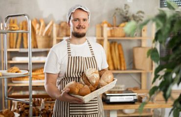 Young man seller holding basket with fresh croissants in bakery