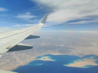 Aerial View of Airplane Wing Over Coastline and Sea, Red Sea, Egypt - A high-resolution aerial photograph taken from an airplane window, showing the aircraft wing above a deep blue sea with a desert c