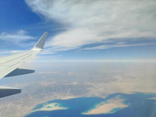 Aerial View of Airplane Wing Over Coastline and Sea, Red Sea, Egypt - A high-resolution aerial photograph taken from an airplane window, showing the aircraft wing above a deep blue sea with a desert c
