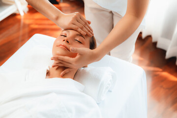 Caucasian woman enjoying relaxing anti-stress head massage and pampering facial beauty skin recreation leisure in dayspa modern light ambient at luxury resort or hotel spa salon. Quiescent