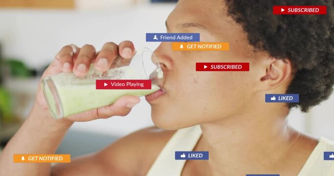 Man sipping pale green drink in kitchen, raising glass making social media icons float for sharing