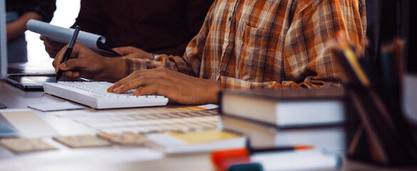 A professional designer is engaged in a digital project at a modern desk, surrounded by papers, colorful markers, and a collaborative team, fostering creativity and innovation. SACTR
