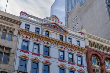 Architectural juxtaposition: ornate historical building stands between aged structure and modern skyscrapers against a cloudy sky © Mujie