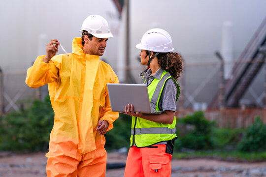 Two environmental engineers in PPE gear reviewing field data on a laptop during coastal inspection, focusing on pollution monitoring, water testing, and hazard evaluation.