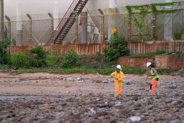 Two environmental specialists in safety gear conduct a field investigation at a polluted coastal site, collecting data and assessing contamination risks near an industrial zone.