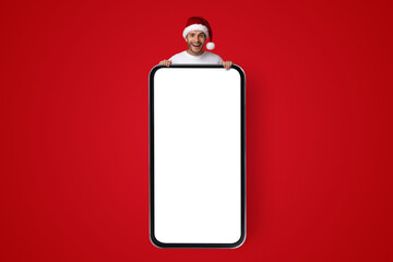 Festive individual wearing a Santa hat smiles while holding a large blank sign. The bright red background adds to the cheerful holiday spirit, inviting creativity and fun.