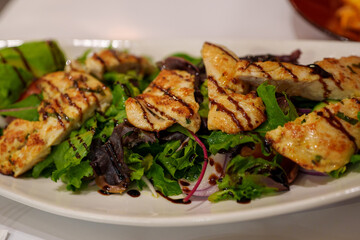 A Platter of Grilled Chicken Salad with Mixed Greens and Balsamic Drizzle on a White Plate