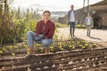 Fototapeta premium Woman farmer planting seeds in the garden on the farm on background of family. Planting seeds and fertilizing the land. Farmer grows organic natural food