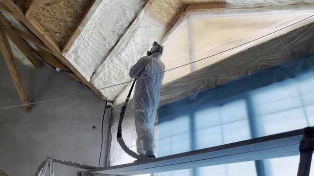 Professional worker spraying polyurethane foam insulation on building roof