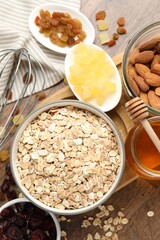 Making granola. Oat flakes in bowl, dried fruits, almond nuts and honey on wooden table, flat lay