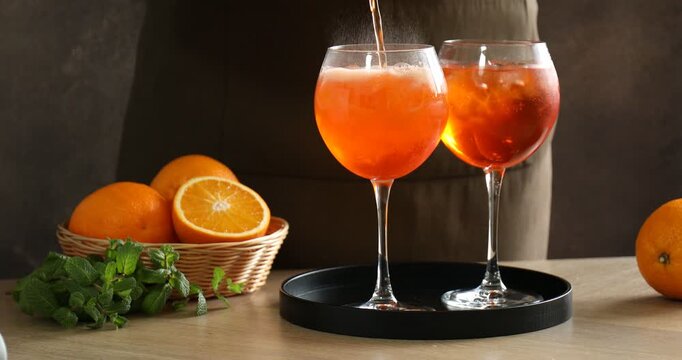 Woman pouring spritzer cocktail into glasses and adding mint at table, closeup