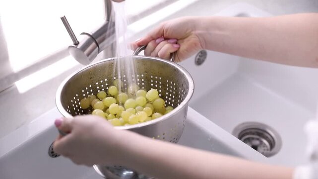 Woman washing grapes in colander at sink, closeup
