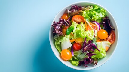 Freshly prepared mixed green salad rests in a white bowl against a light blue background