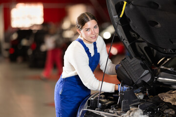 Female mechanic checks the car and carries out maintenance. Professional mechanic checks the engine and oil under the hood of the car