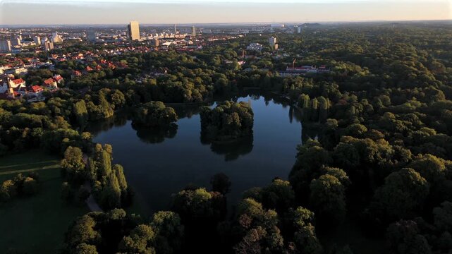 Luftaufnahme vom Englischen Garten mit Kleinhesseloher See in Munchen, Bayern. Historischer Park mit Inseln, Wasser, Seehaus und Natur. Beliebte Sehenswuerdigkeit und Ausflugsziel in Deutschland