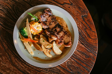 Top view of grilled steak served with potato wedges and colorful vegetables on a rustic wooden table. Warm lighting, authentic food styling perfect for menu design, restaurant promotion, and culinary
