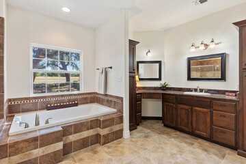 A bathroom that features a tub, a sink, cabinets, and a window