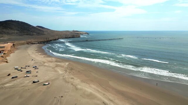 Aerial view of Puerto Eten in Chiclayo, Lambayeque, showing the fishing pier, sandy beach, and calm Pacific coastline under clear skies