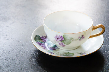 Empty teacup and saucer painted with purple lilac flowers, copy space on left