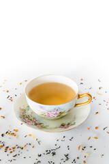 Tea in teacup on saucer, white background with tea leaves in foreground, copy space above