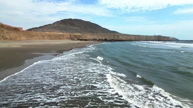 Aerial view of Puerto Eten in Chiclayo, Lambayeque, showing the fishing pier, sandy beach, and calm Pacific coastline under clear skies