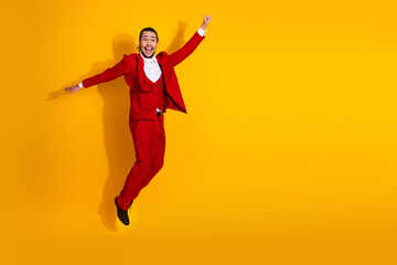 Fototapeta premium Energetic man in red suit leaps against bright yellow background creating a playful dynamic fashion moment perfect for celebration imagery