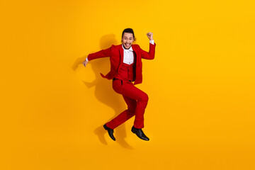 Energetic man in red suit leaps against bright yellow background creating a bold fashion moment for ads and festive campaigns