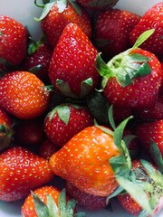 A close-up, overhead view of a pile of fresh, ripe strawberries with green stems