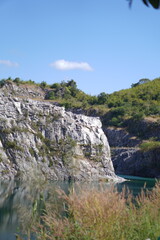 Obraz premium Blue Lagoon Phuman Khon Kaen: Majestic gray limestone cliff beside a clear turquoise water pond, with perfect reflection under the summer sky