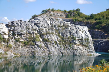 Blue Lagoon Phuman Khon Kaen: Majestic gray limestone cliff beside a clear turquoise water pond, with perfect reflection under the summer sky