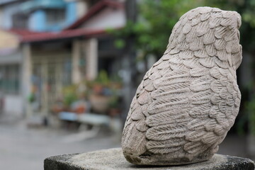 Stone owl sculpture in focus with blurred house background, outdoor art piece, serene vibe