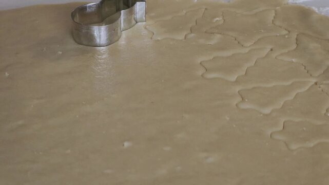 A close up of a Snowman shaped cookie cutter being used to make shaped Christmas cookies on a sheet of cookie dough.