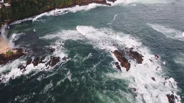 Powerful ocean waves forcefully crashing against rocky tropical coastline, revealing raw natural energy and pristine vegetation from dramatic aerial perspective in Mirissa, Sri Lanka