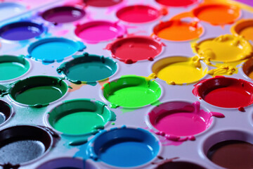 Close up view of used watercolor paint palette with bright colorful circular pans including pink blue and yellow shades for creative art education concept