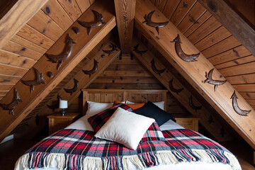 Cozy rustic attic bedroom interior with a wooden ceiling, moon decorations, and a bed with a plaid blanket in a warm mountain chalet or cabin design